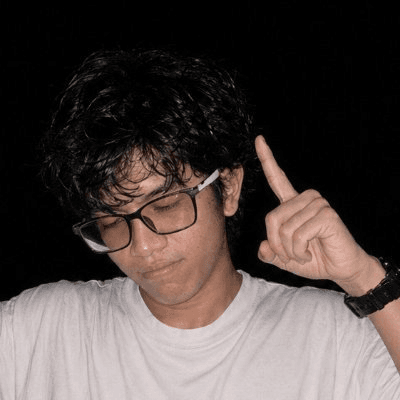Jari in a white shirt against a dark background, raising one finger.